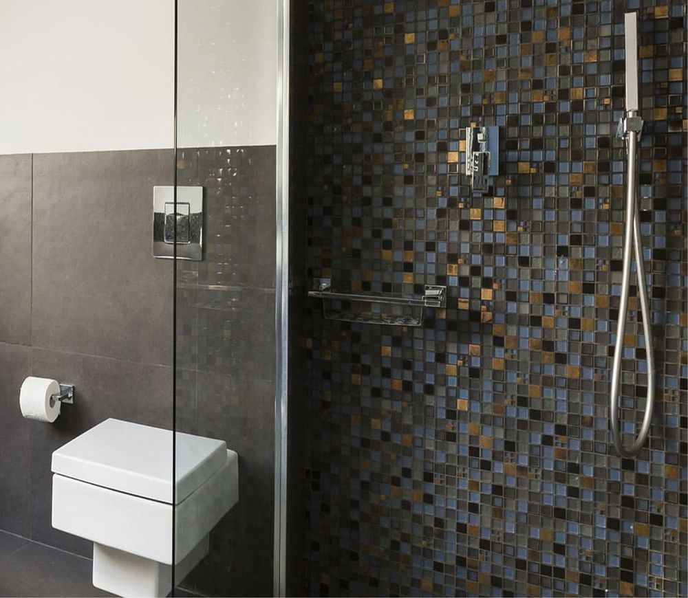 Modernes Badezimmer mit Mosaikfliesen, Wand-WC und Glasduschabtrennung.